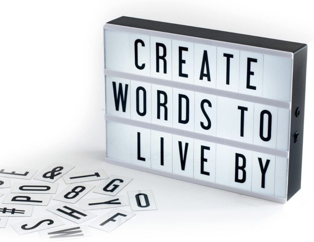 Caja de luz estilo cine con el mensaje CREATE WORDS TO LIVE BY y letras sueltas sobre una mesa blanca.