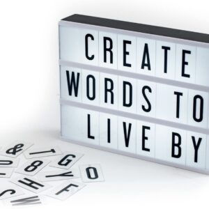Caja de luz estilo cine con el mensaje CREATE WORDS TO LIVE BY y letras sueltas sobre una mesa blanca.