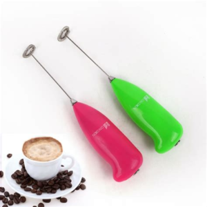 Dos batidores de mano eléctricos en colores rosa y verde junto a una taza de café sobre granos de café.
