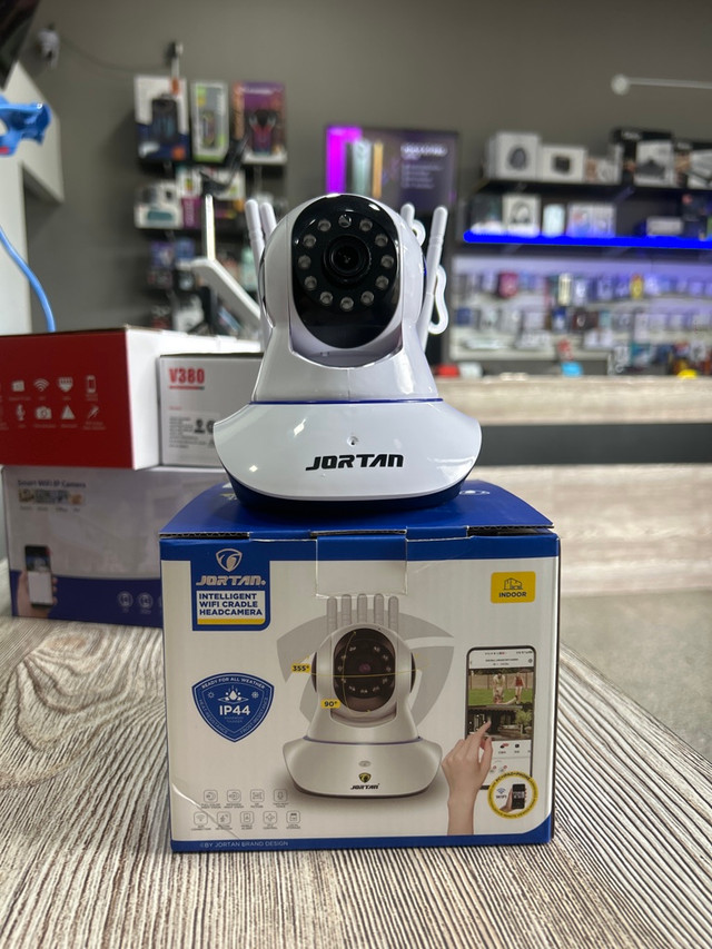 Cámara de seguridad Wi-Fi Jortan blanca sobre su caja de empaque en una tienda de tecnología.
